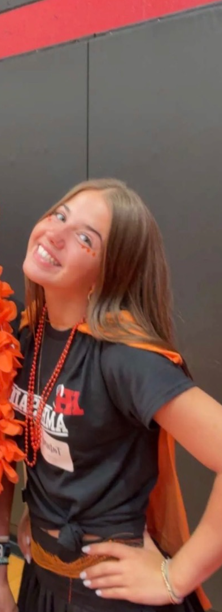 Tatum at a school spirit event wearing an orange cape and a red beaded necklace
