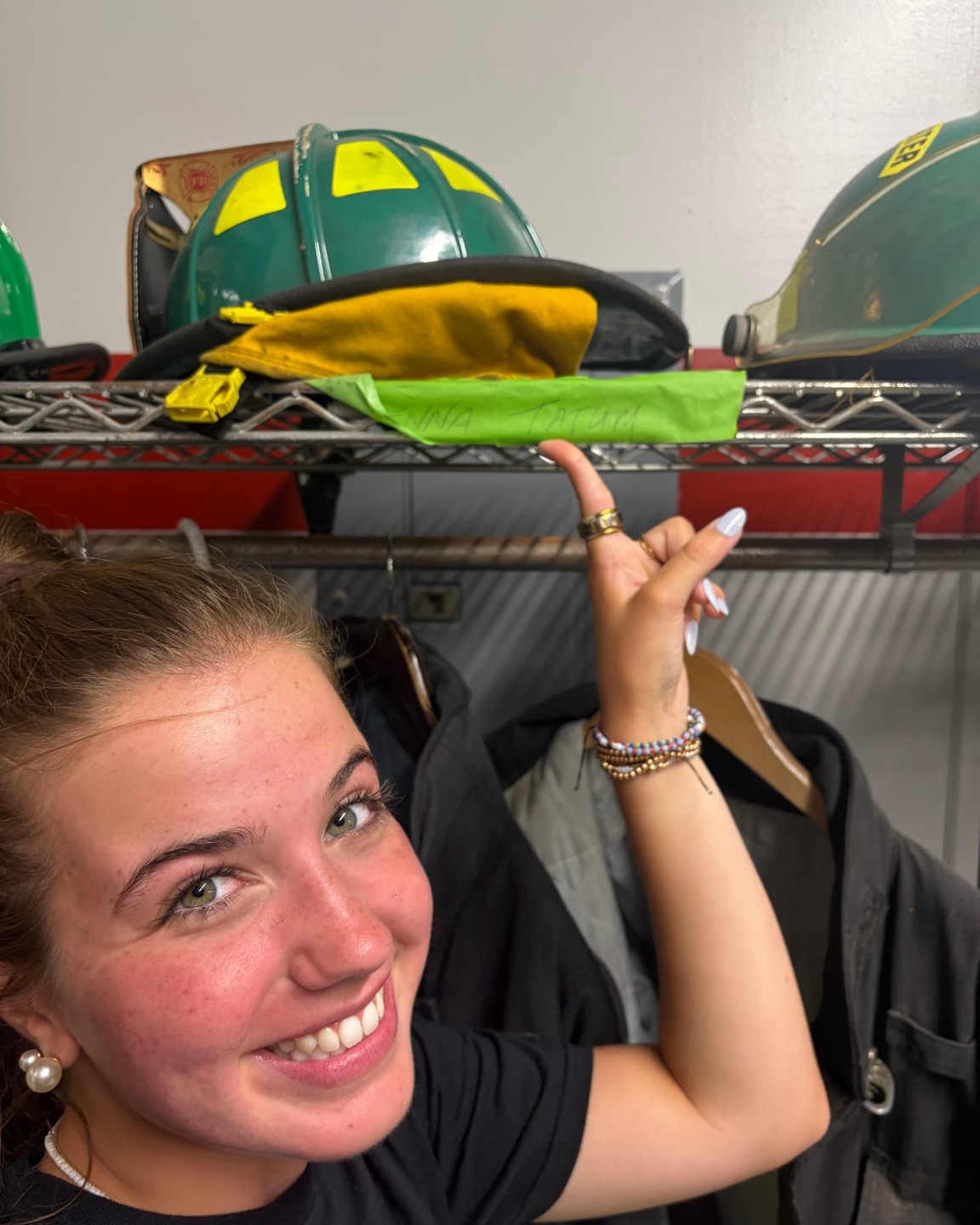 Tatum pointing up at her name taped to the gear shelf in the firehouse locker room