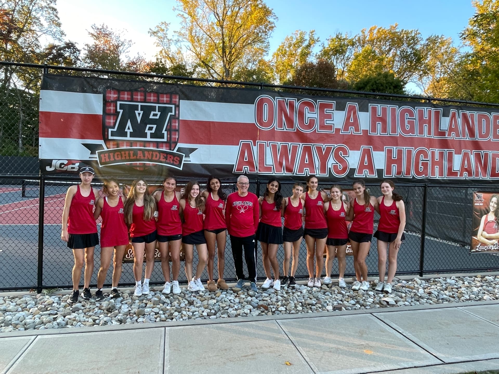 The North Highlands girls' tennis team and their coach in front of the Once a Highlander, Always a Highlander banner