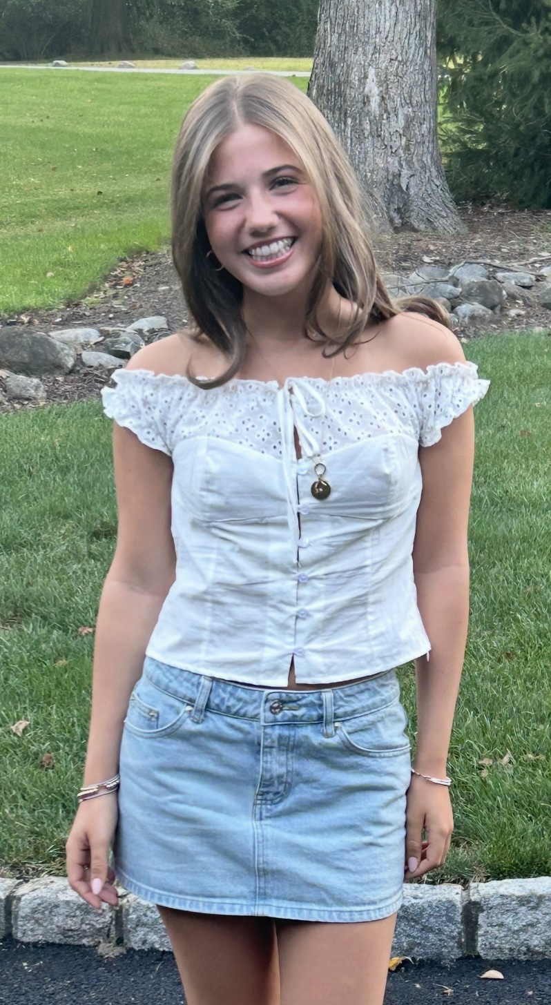 Tatum standing outdoors in a white off-the-shoulder blouse and a denim skirt