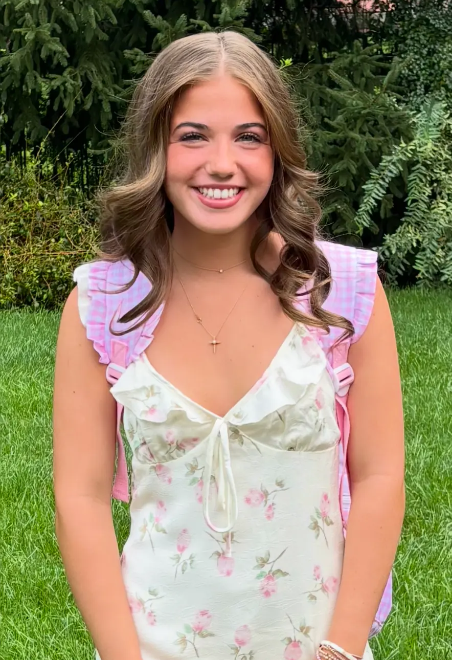 Tatum smiling outdoors in a floral dress with a pink gingham backpack