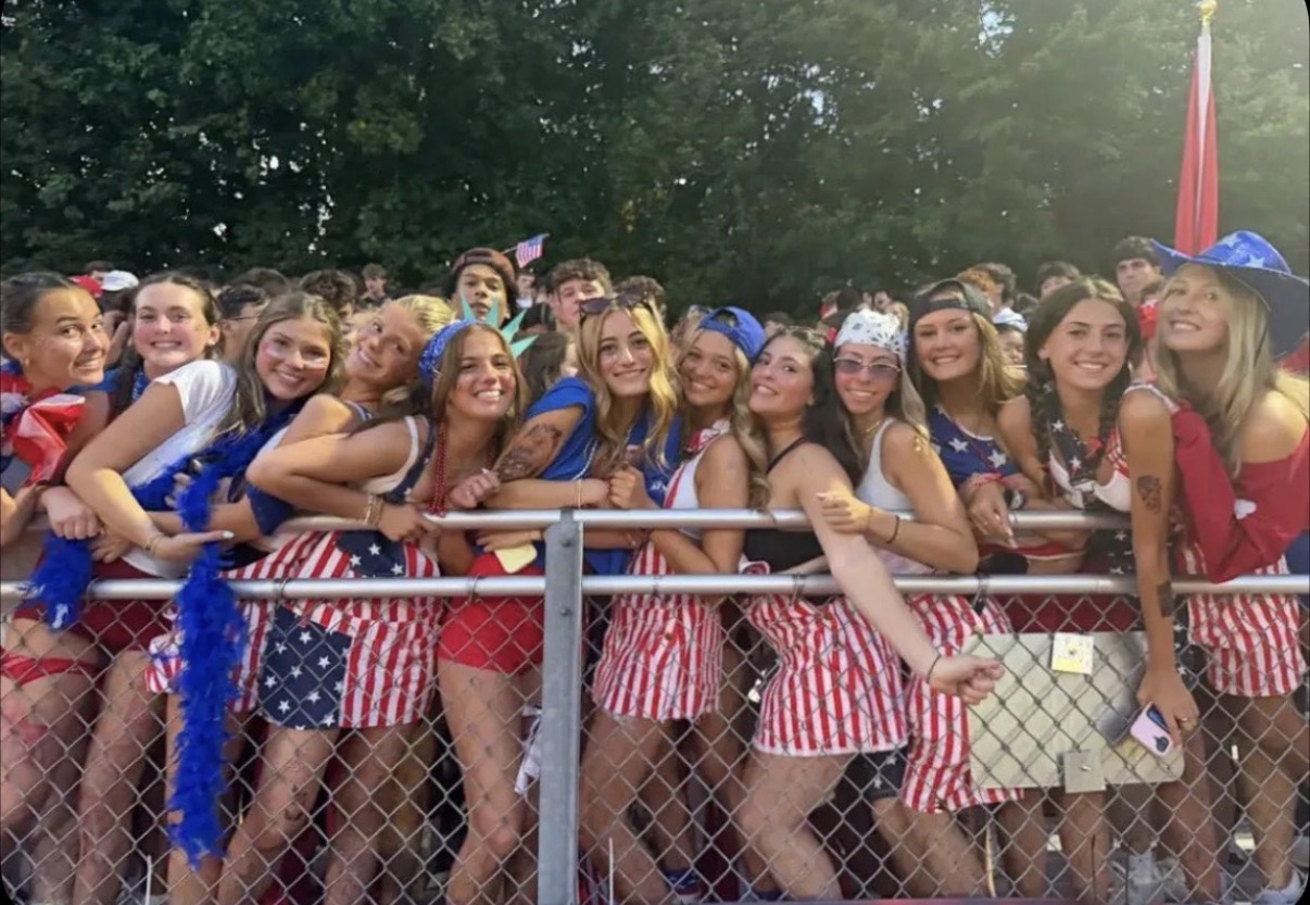 Tatum and friends in red, white and blue outfits leaning on a fence railing at an outdoor game