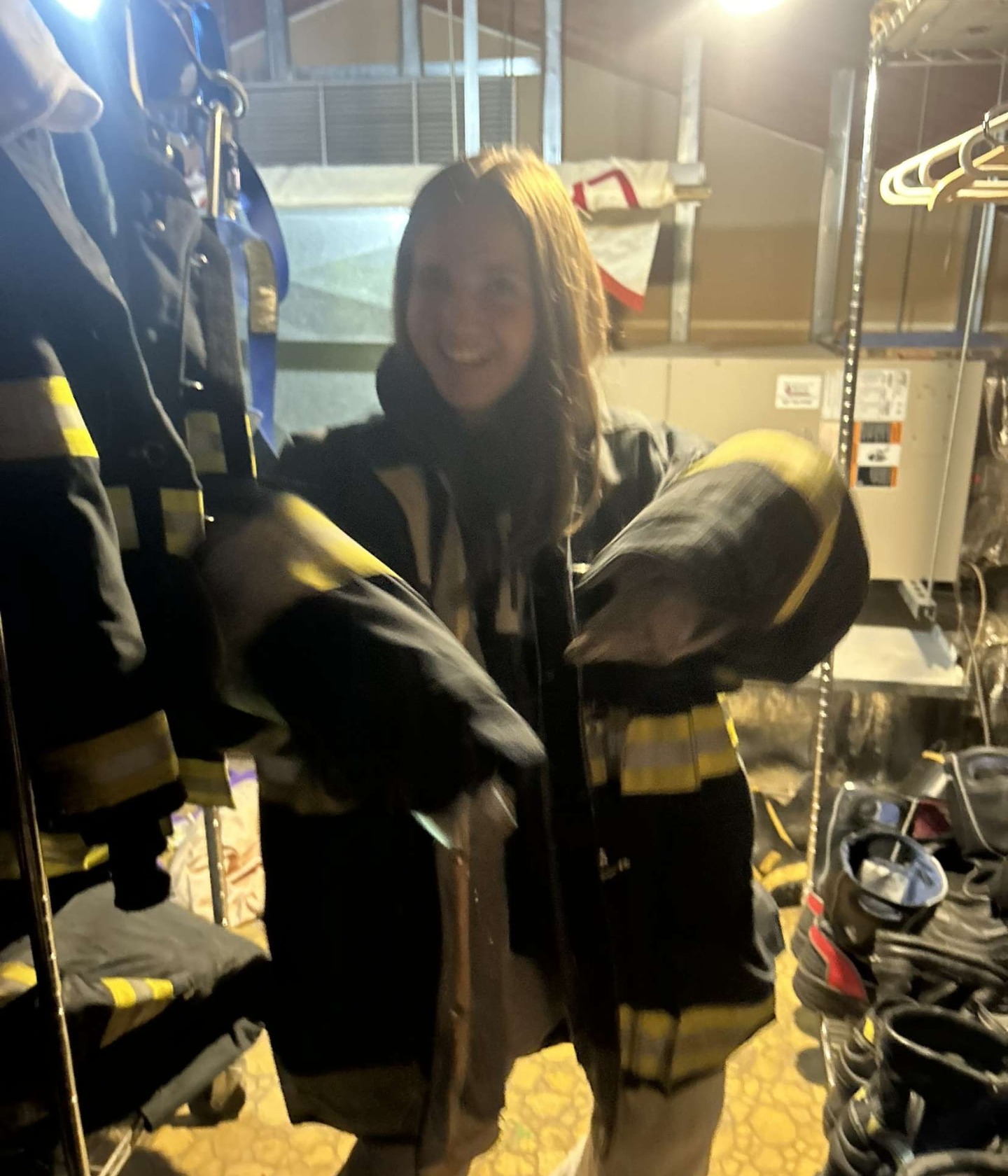 Tatum smiling while trying on an oversized firefighter turnout coat in the gear room