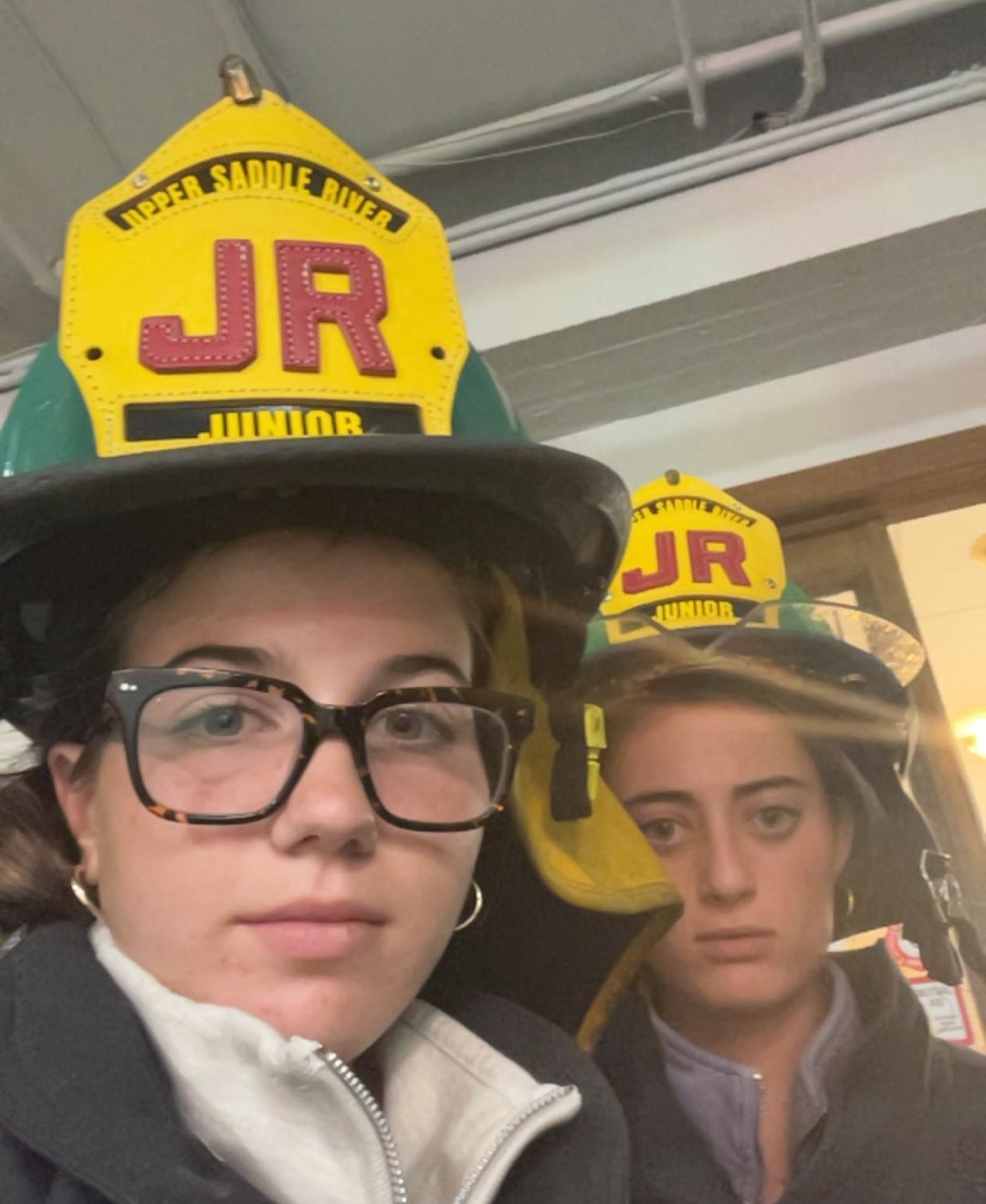 Two USRFD junior firefighters in turnout coats and junior helmets inside the firehouse